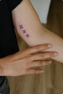 Small purple butterfly trio tattoo on the upper arm