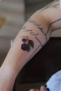 Blackwork berries tattoo with cursive script on the forearm